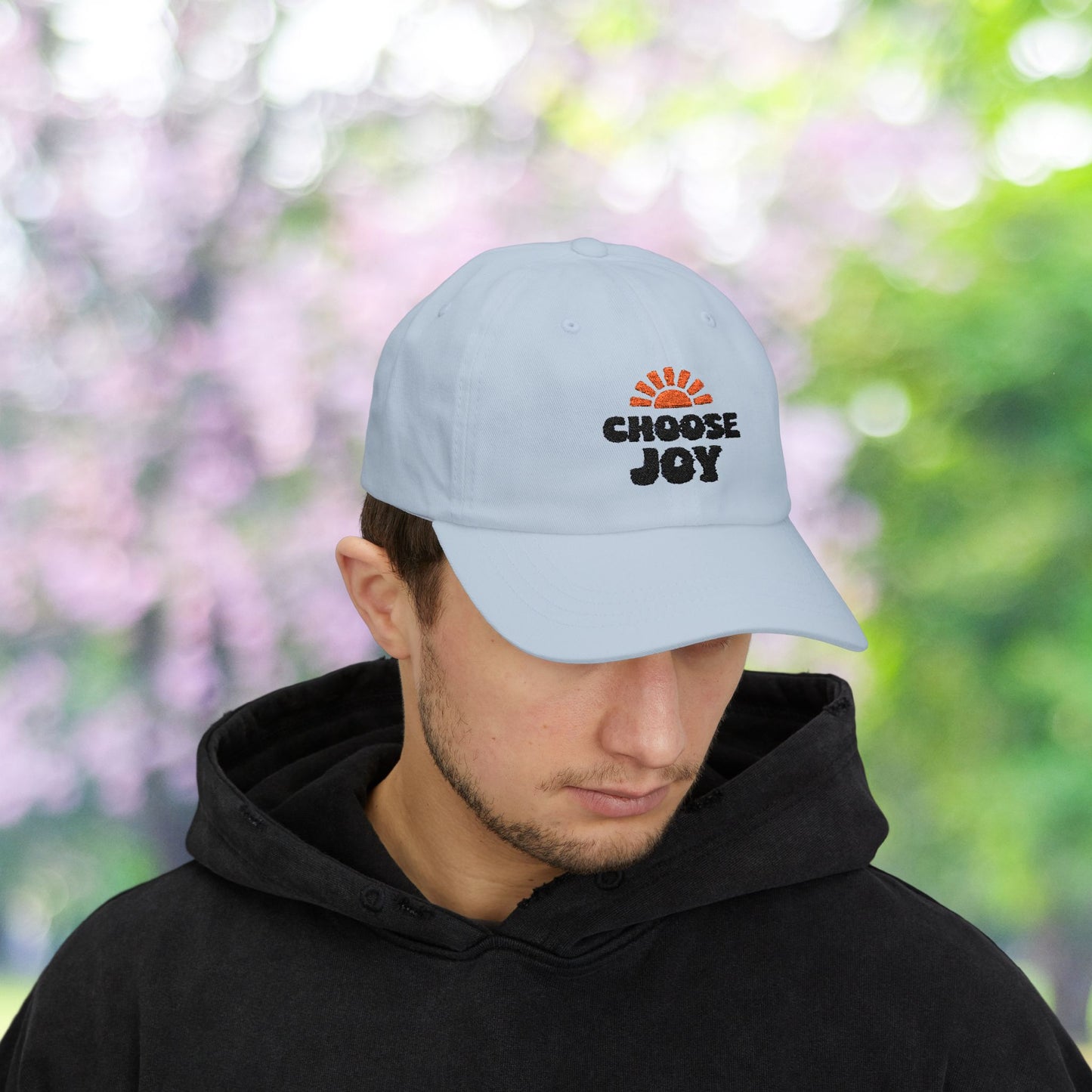 Man wears Choose Joy baseball cap with sun graphic.